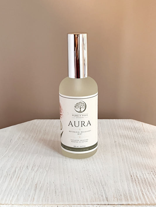 Aura  Botanical Recovery Mist by Purely Pixie Apothecary in a frosted glass bottle with a silver cap, displayed on a white wooden surface against a soft blush background. Hydrating botanical essence for refreshing and replenishing skin.